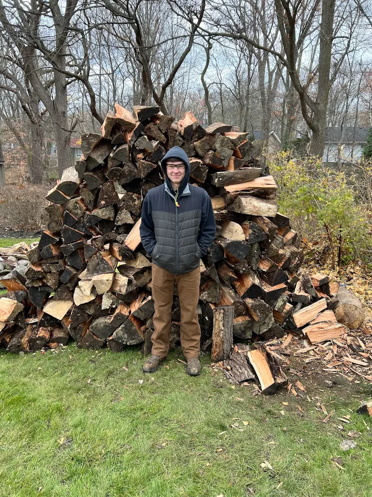 A Clips crew member standing beside a split and stacked woodpile